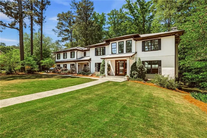 White stucco exterior with dark trim and shutters, prominent front entry with glass-paneled double doors, and a covered porch supported by columns