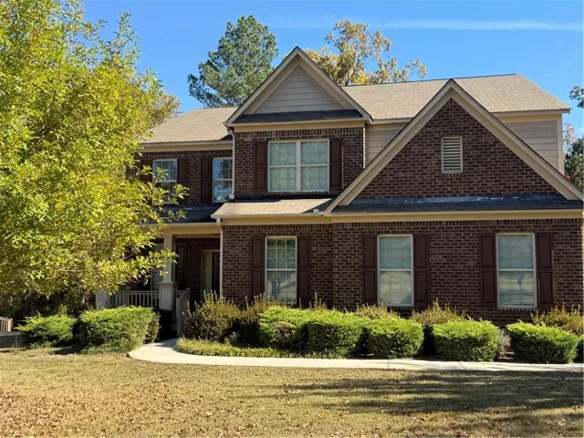 View of front of house featuring brick siding, a porch, a front lawn, and roof with shingles