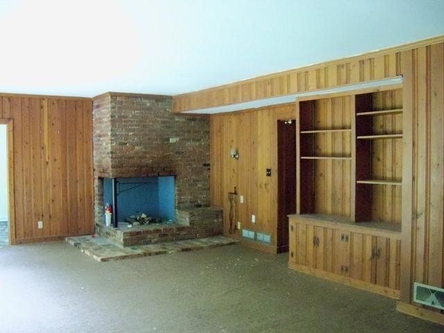 Unfurnished living room featuring wooden walls, built in features, a fireplace, and brick wall