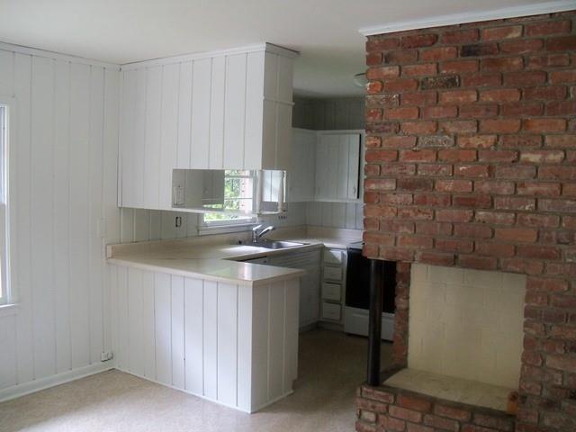 Kitchen featuring brick wall, light carpet, kitchen peninsula, white cabinets, and sink