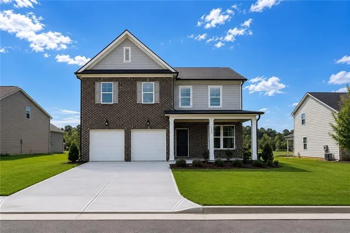 Two-story residence featuring brick and siding exterior, a covered front porch with white columns, an attached two-car garage, concrete driveway, and a landscaped front yard with green grass