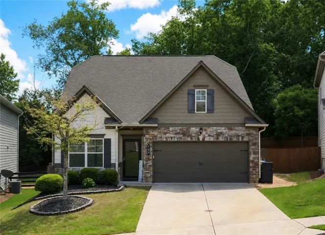 Craftsman-style exterior featuring a stone accent façade, a two-car garage, and a neatly landscaped front yard