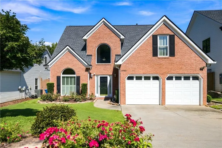 Brick exterior featuring a two-car garage, arched windows, and a landscaped front yard with established plantings