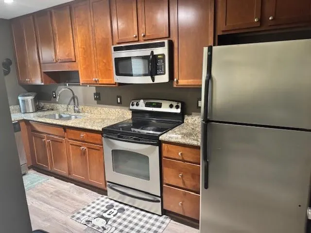 Kitchen featuring stainless steel appliances, light stone countertops, wood finish cabinetry, and light wood-style flooring