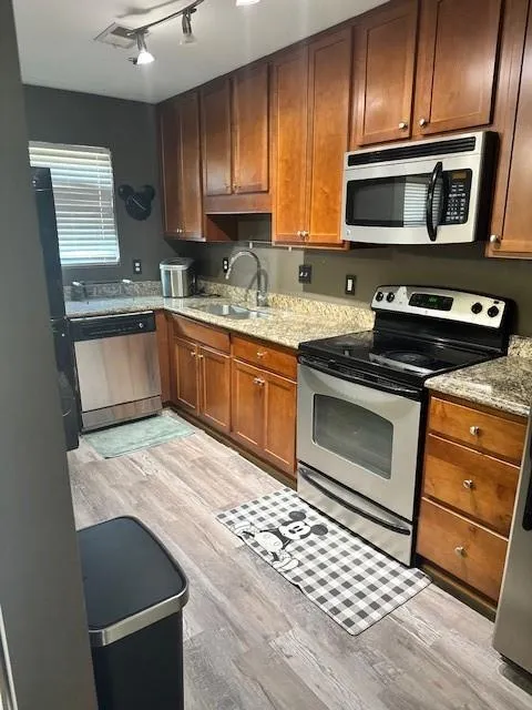 Kitchen featuring stove, light stone counters, stainless steel microwave, dishwashing machine, and light wood finished floors