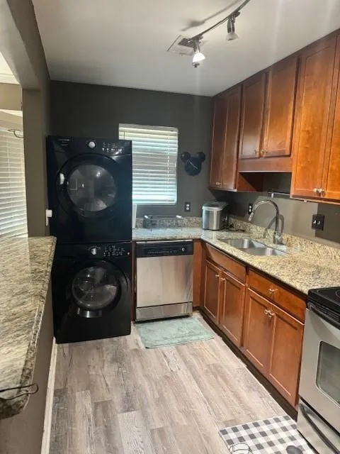 Kitchen with range, dishwasher, light stone counters, stacked washer and clothes dryer, and light wood-style floors