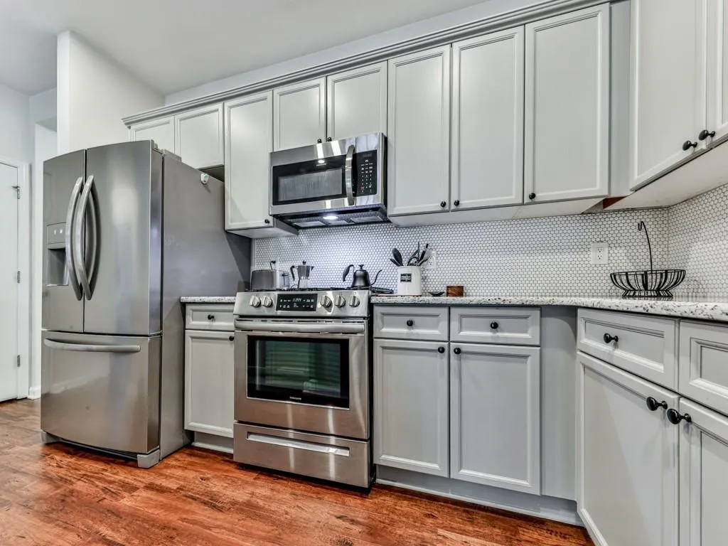 Kitchen with appliances with stainless steel finishes, backsplash, wood finished floors, and light stone countertops
