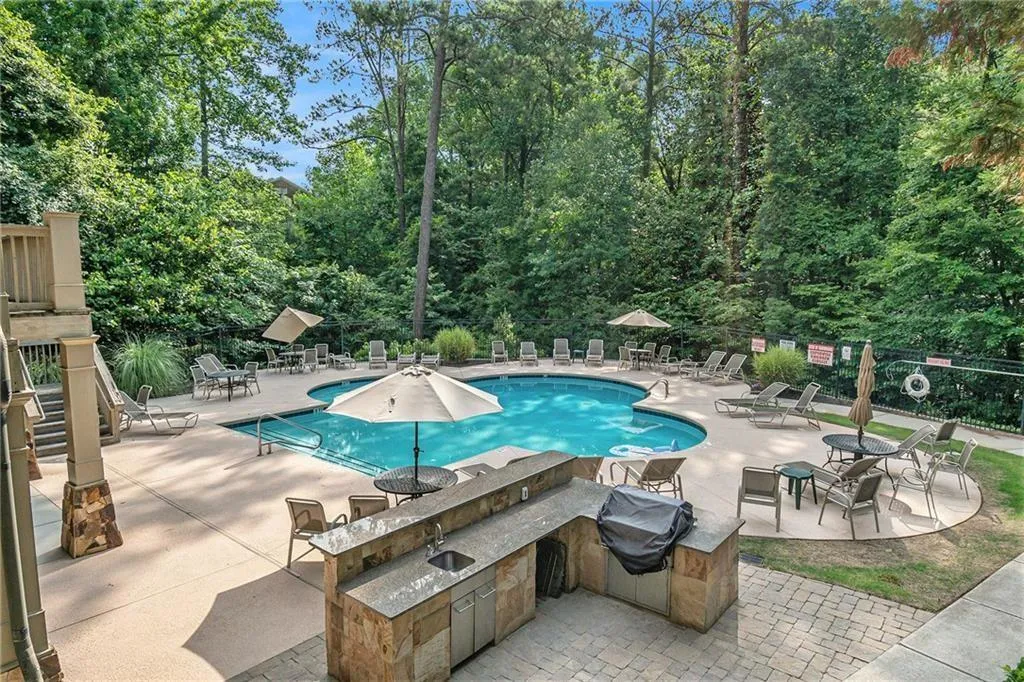 Community pool featuring a patio, view of scattered trees, and exterior kitchen