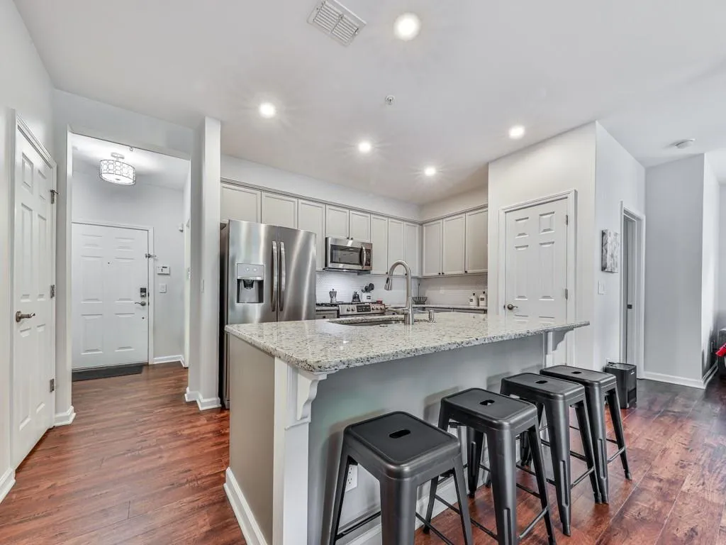Kitchen featuring dark wood finished floors, a breakfast bar, a center island with sink, light stone counters, and stainless steel microwave