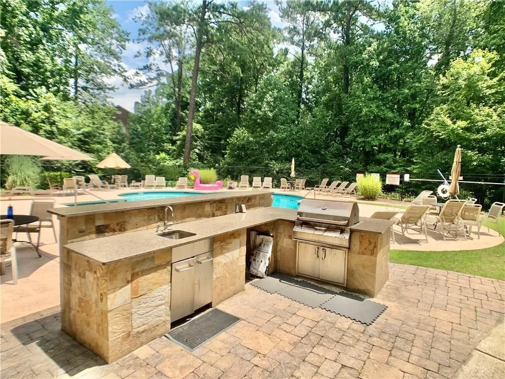 View of patio / terrace with exterior kitchen, view of scattered trees, a community pool, and an outdoor bar