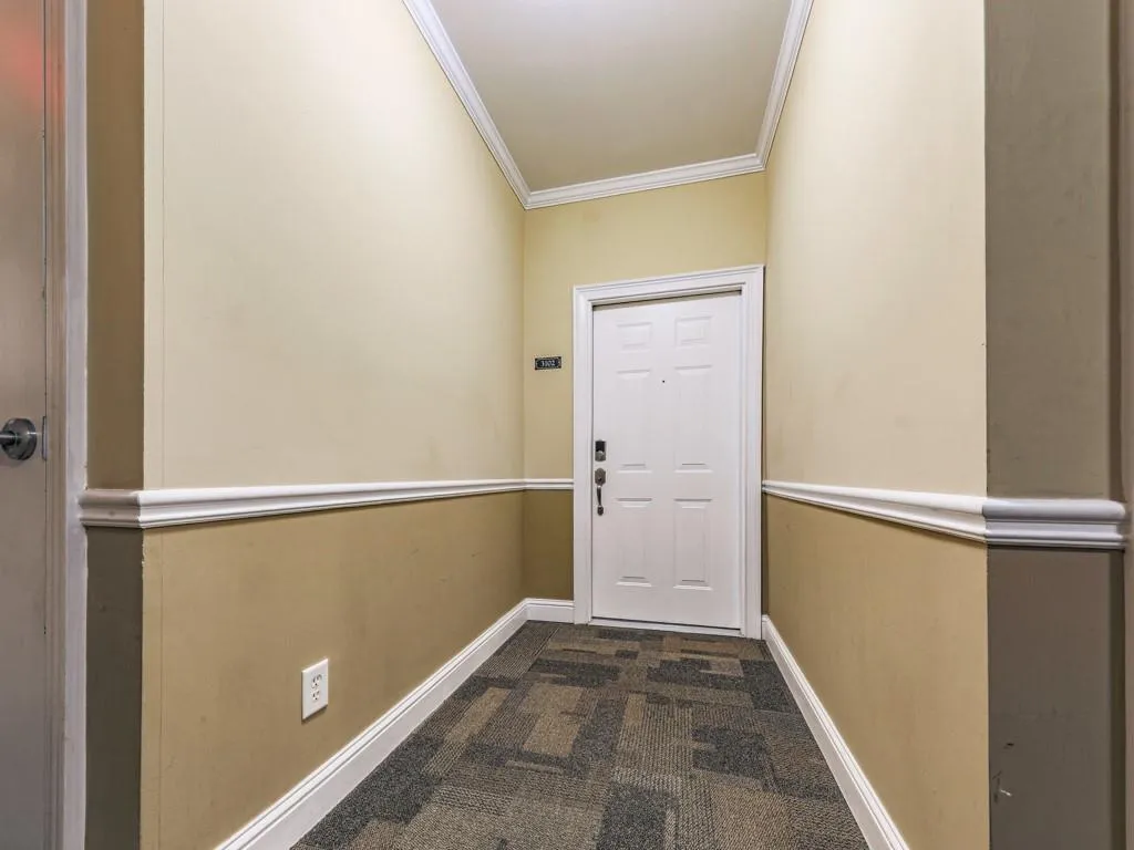 Doorway to outside featuring ornamental molding and dark carpet