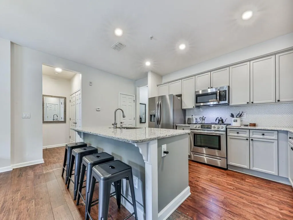 Kitchen featuring decorative backsplash, appliances with stainless steel finishes, dark wood-style floors, a kitchen island with sink, and recessed lighting