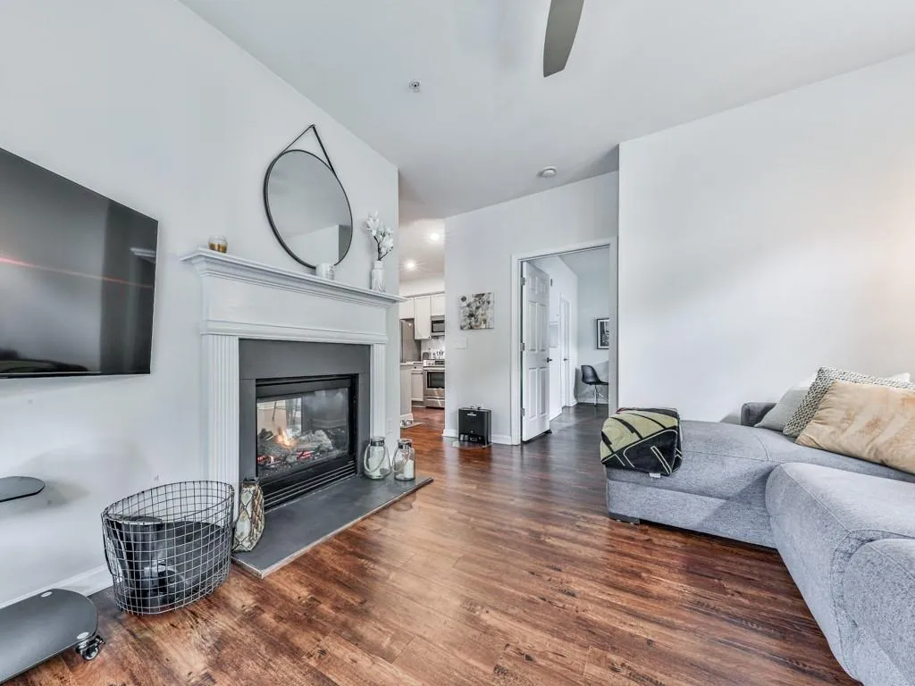 Living area with dark wood-type flooring, a glass covered fireplace, and a ceiling fan