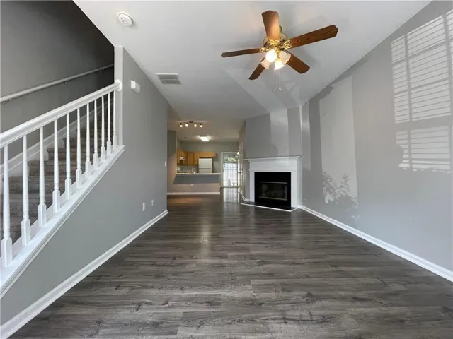 Wood-finish flooring, white mantel fireplace, ceiling fan with integrated lighting, and a white staircase with carpeted treads