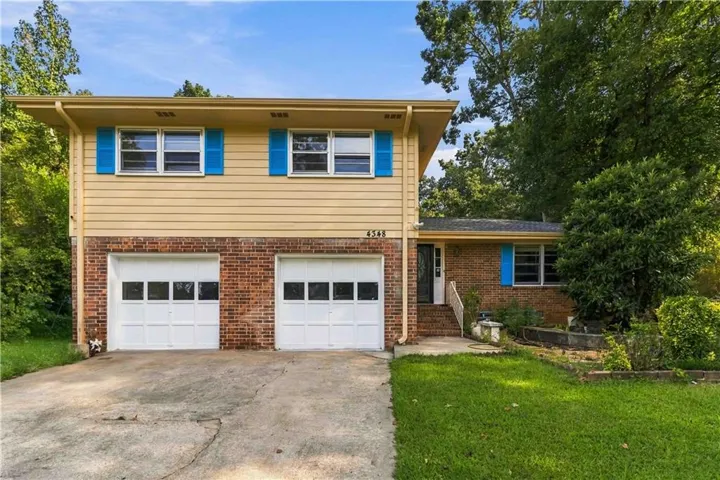 Split-level residence featuring a brick and siding exterior, two garage doors with window inserts, a concrete driveway, and mature landscaping
