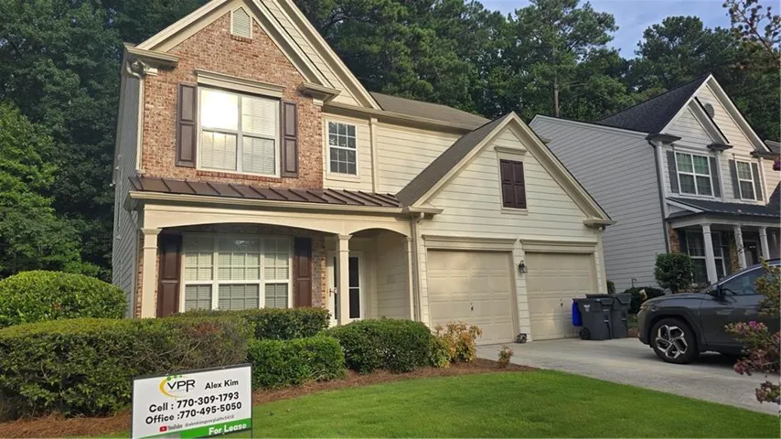 Traditional-style exterior with brick and siding facade, covered front porch, dark shutters, two-car garage, and established landscaping