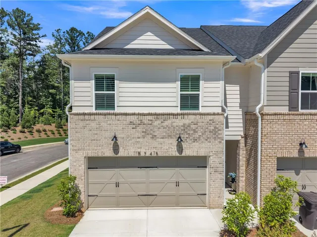 Two-story townhouse exterior featuring a two-car garage, light-colored brick facade, horizontal siding, and dark shingle roofing