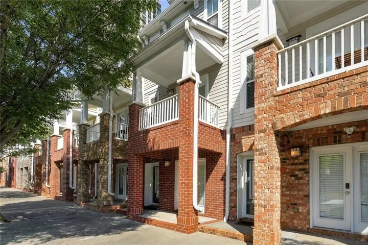Exterior featuring brick and stone facades, white siding, individual balconies with white railings, and mature trees providing natural shade