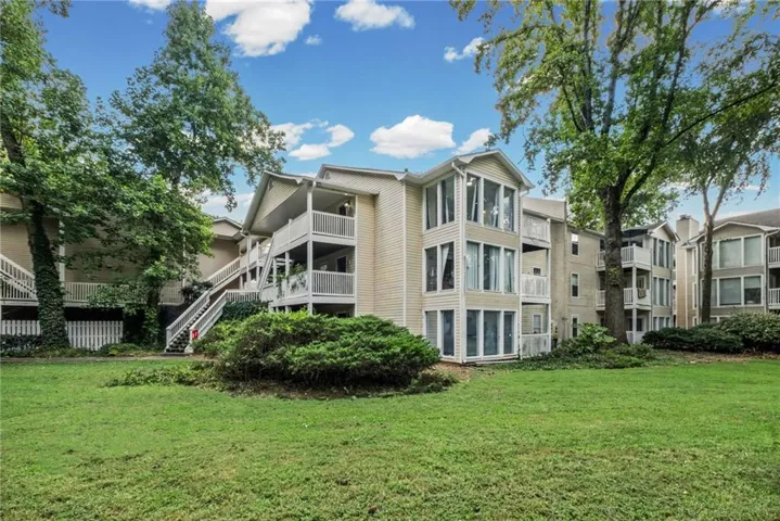 Multi-story building exterior with light-colored siding, multiple balconies with white railings, and large windows