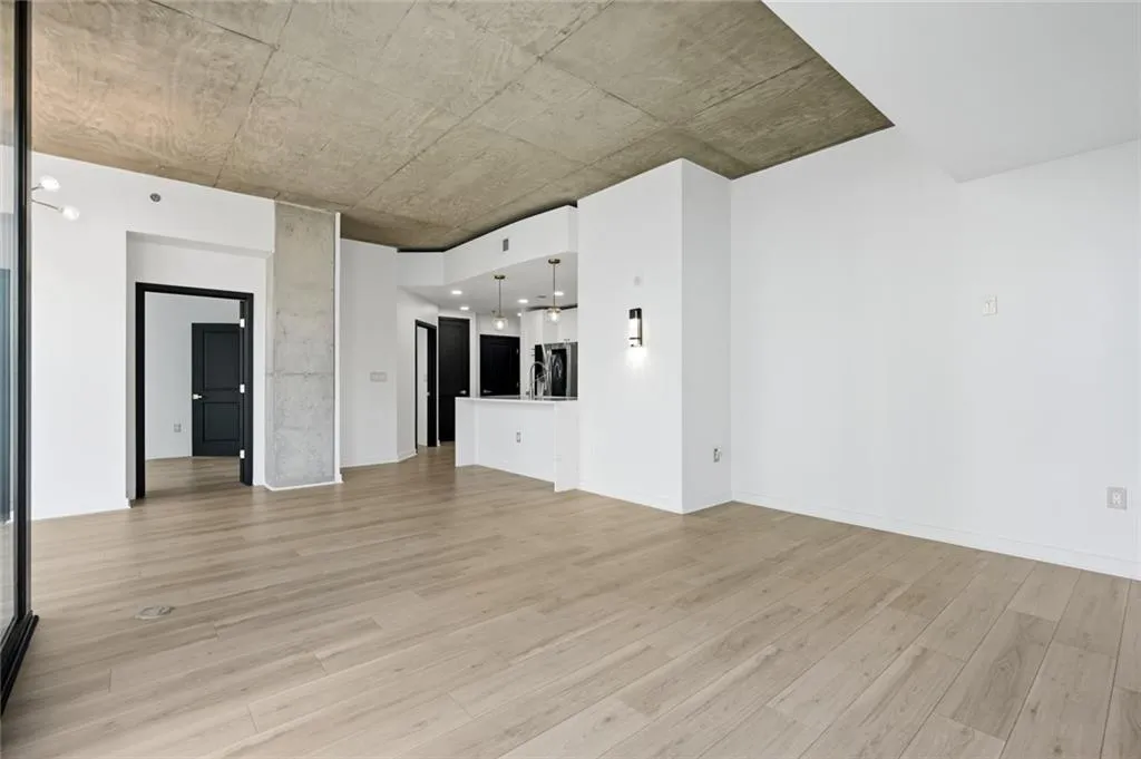 Open-concept interior featuring light wood-finish flooring, white walls, and an exposed concrete ceiling