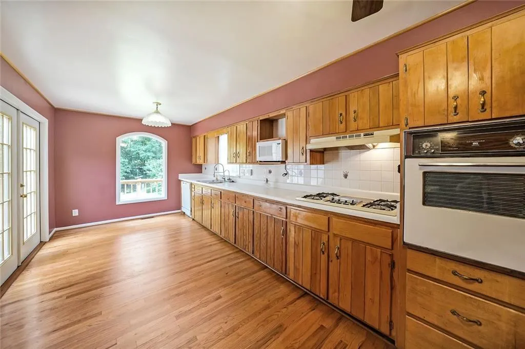 Kitchen featuring white appliances, under cabinet range hood, a sink, light wood-style flooring, and brown cabinetry