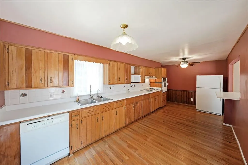 Kitchen with white appliances, a sink, light wood-type flooring, a ceiling fan, and light countertops