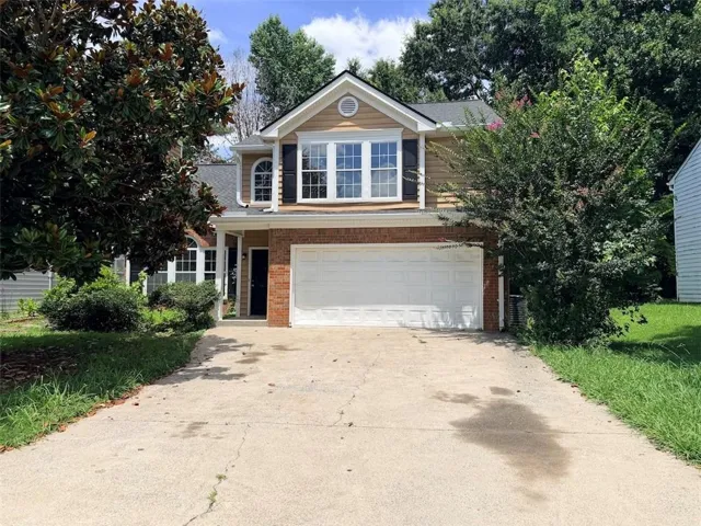 Two-story residence featuring a brick facade, tan siding, an attached two-car garage, and a concrete driveway