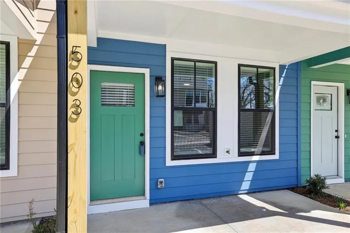 Vibrant blue horizontal siding with white trim, green paneled entry door with transom window, black exterior wall sconce, and black-framed windows