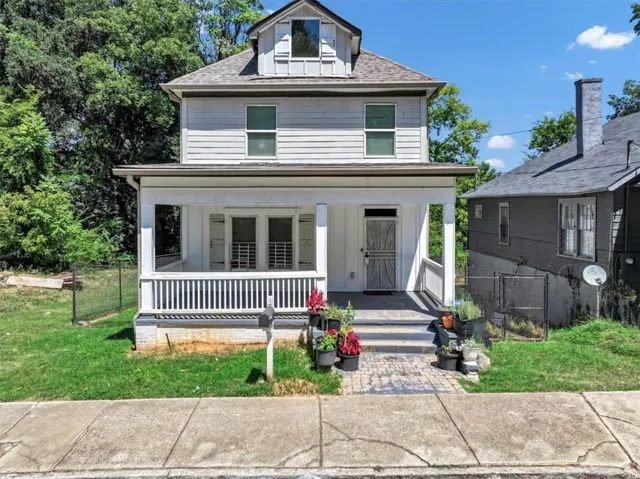 Two-story residence featuring a covered front porch with white railings, a front-facing dormer, and a paved walkway