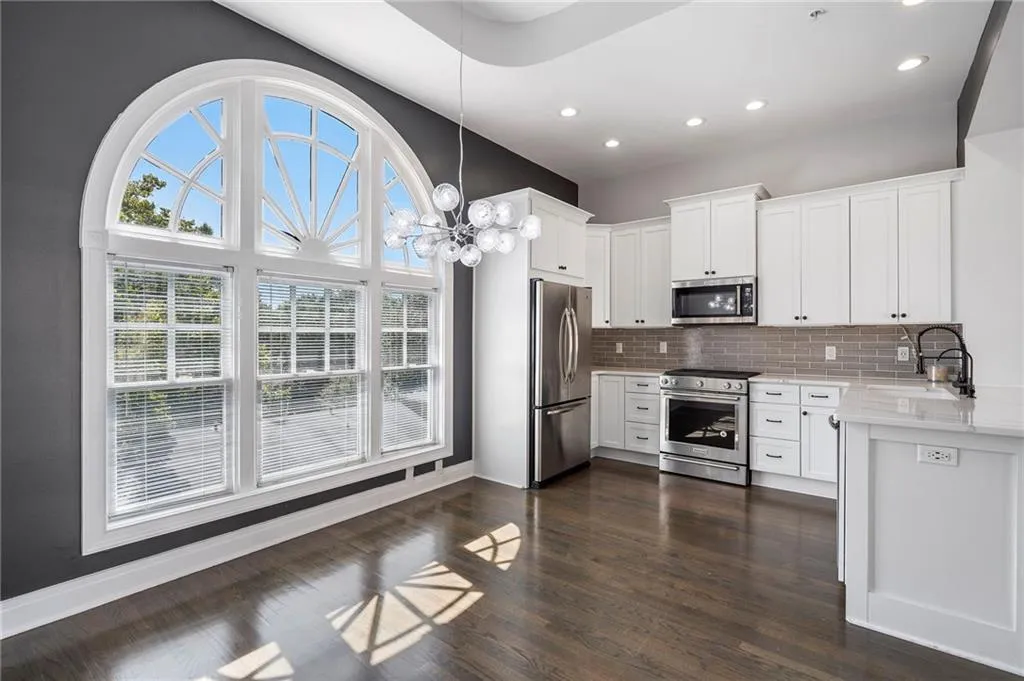 Kitchen with a chandelier, appliances with stainless steel finishes, white cabinetry, light stone counters, and hanging light fixtures Kitchen with a chandelier, appliances with stainless steel finishes, white cabinetry, light stone counters, and hanging light fixtures
