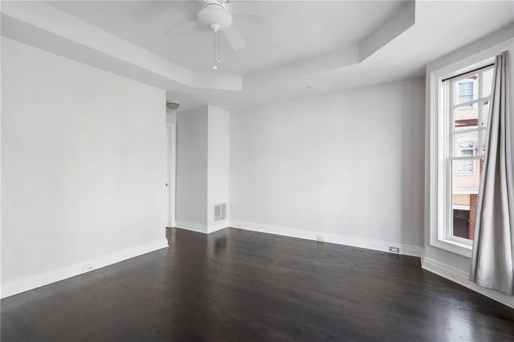 Empty room with a raised ceiling, dark wood-style floors, and a ceiling fan Empty room with a raised ceiling, dark wood-style floors, and a ceiling fan