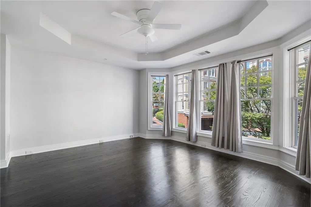 Unfurnished room with a tray ceiling, dark wood-style flooring, and a ceiling fan Unfurnished room with a tray ceiling, dark wood-style flooring, and a ceiling fan