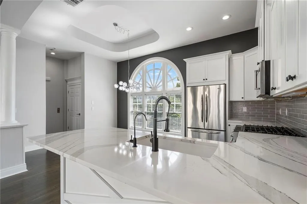 Kitchen featuring light stone countertops, white cabinets, stainless steel appliances, dark wood-style floors, and a tray ceiling Kitchen featuring light stone countertops, white cabinets, stainless steel appliances, dark wood-style floors, and a tray ceiling