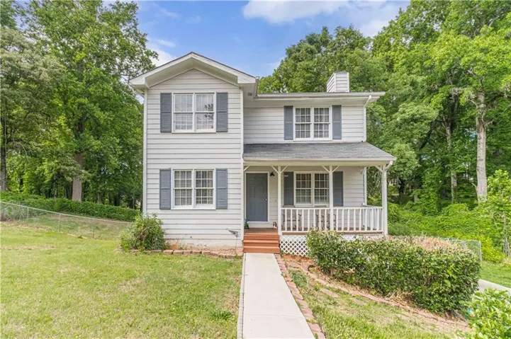 Two-story property featuring light siding, a covered front porch with white railing, blue shutters, a front door, and a concrete walkway