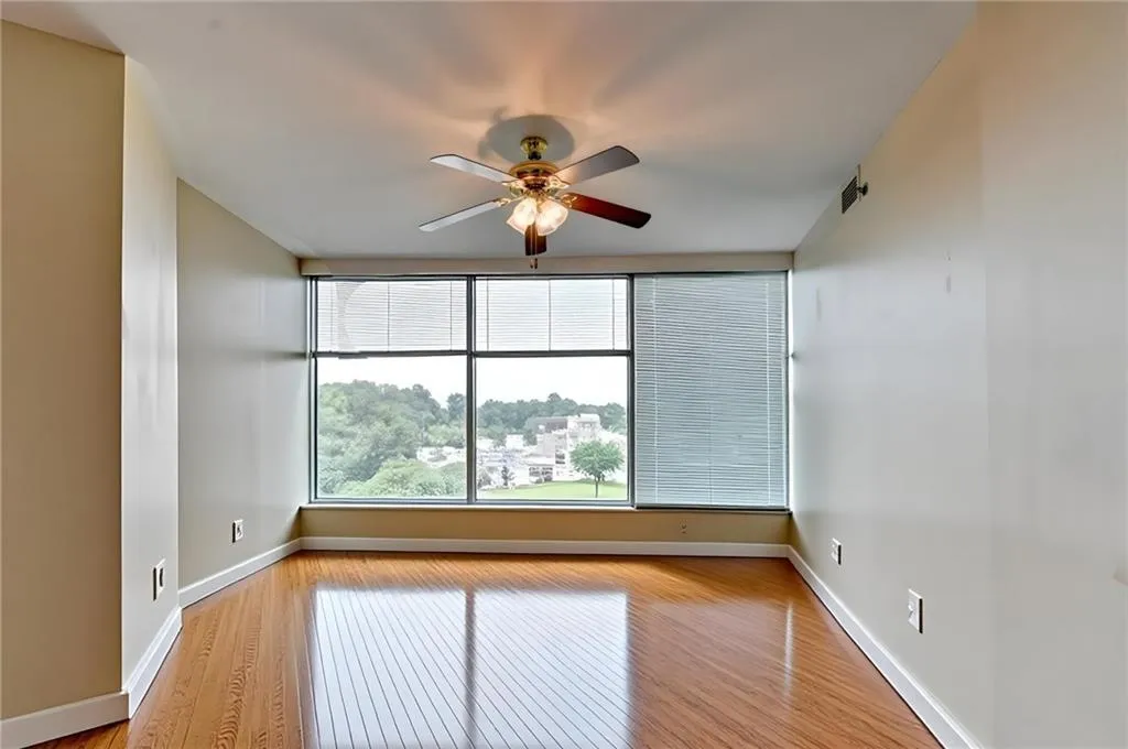 Expansive window wall with horizontal blinds, wood-finish flooring, and a ceiling fan with integrated lighting