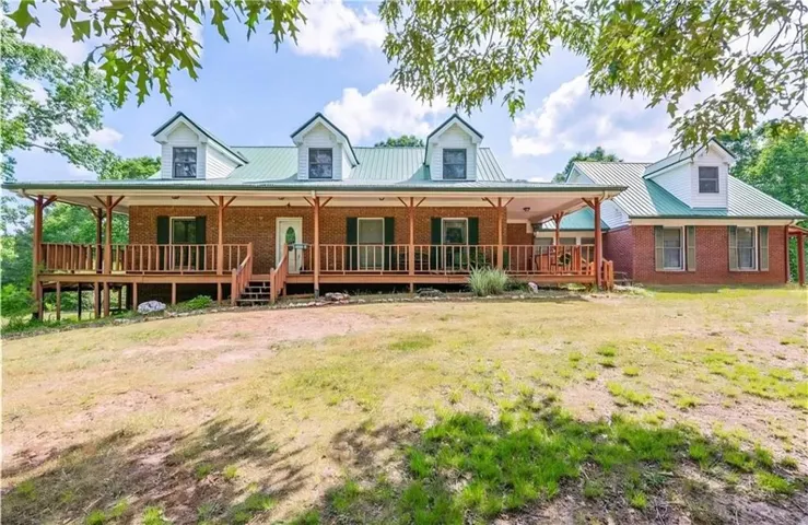 Brick exterior with a green metal roof, a full-length covered porch, and multiple dormer windows