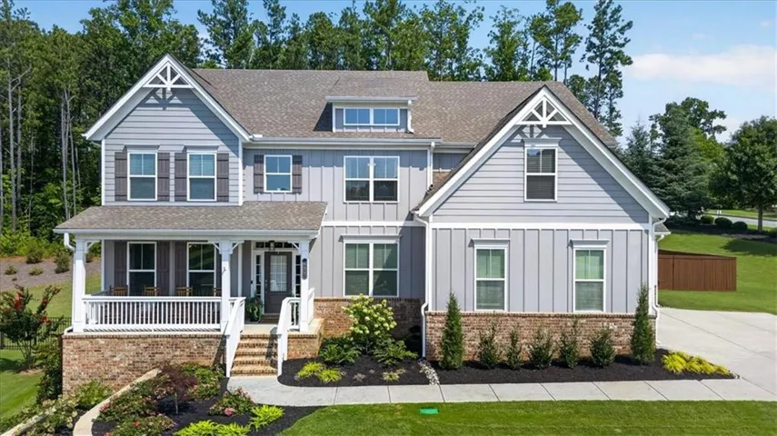 Two-story residence featuring light gray siding, dark gray shutters, a covered front porch with white railing, brick accents, and a landscaped front yard with a concrete walkway