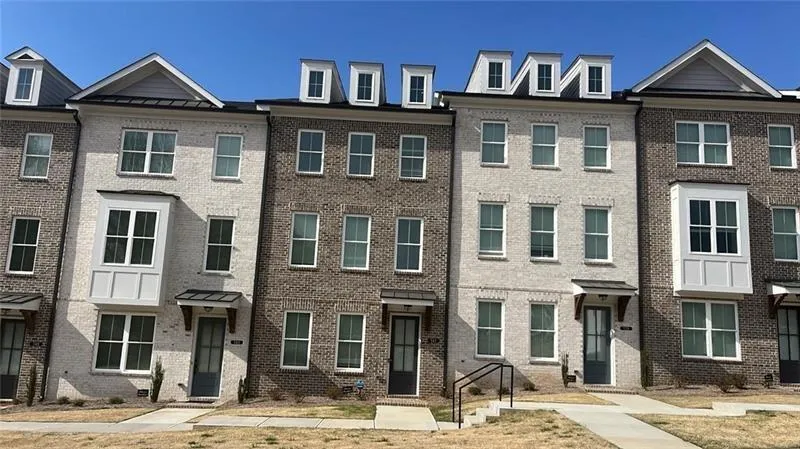 Contemporary townhome facade featuring a three-story design with a light-colored brick exterior