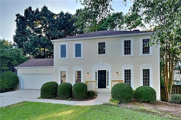 Stucco exterior with multiple windows, attached garage, and established landscaping