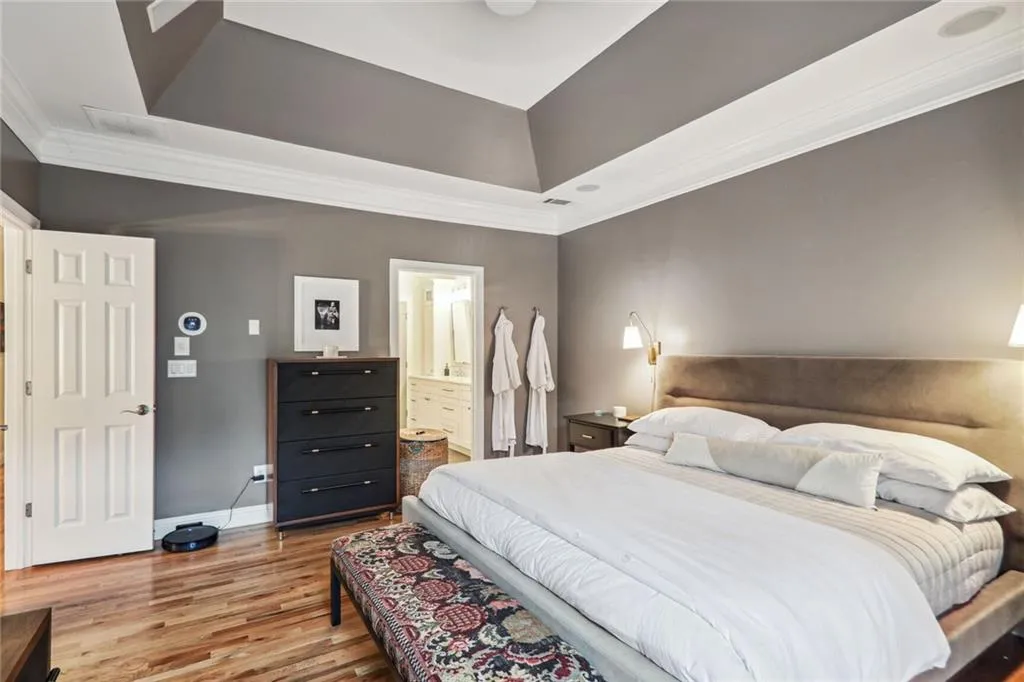 Bedroom featuring hardwood / wood-style flooring, a tray ceiling, crown molding, and ensuite bathroom
