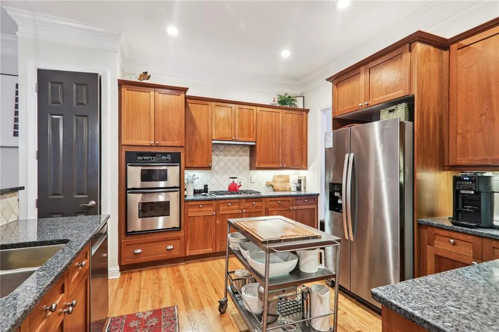 Kitchen with tasteful backsplash, light hardwood / wood-style flooring, dark stone countertops, stainless steel appliances, and ornamental molding