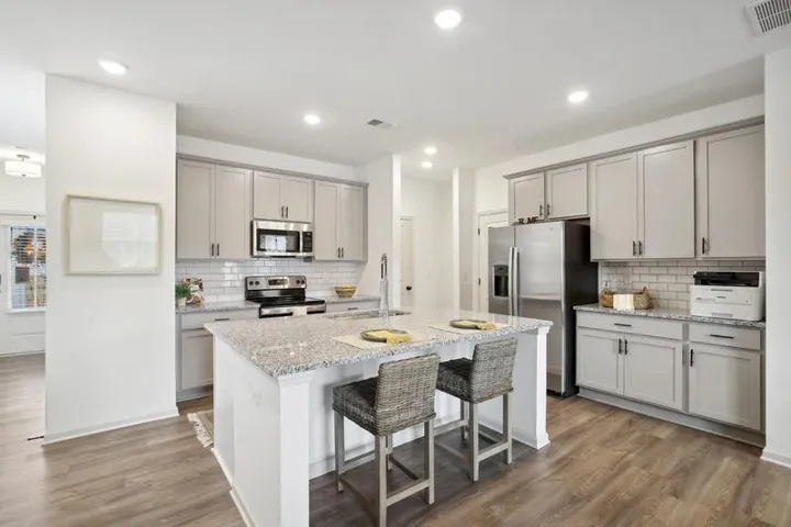 Kitchen with stainless steel appliances, light stone countertops, a kitchen island with sink, dark wood-type flooring, and gray cabinetry
