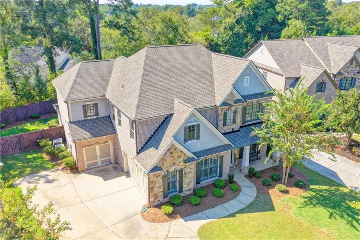 Multi-level residence featuring a shingle roof, brick exterior, stone façade accents, and a concrete driveway