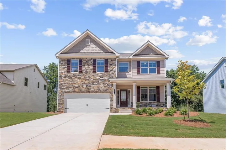 Two-story residence featuring a stone and siding facade, a covered front porch with columns, a two-car garage, and mature landscaping