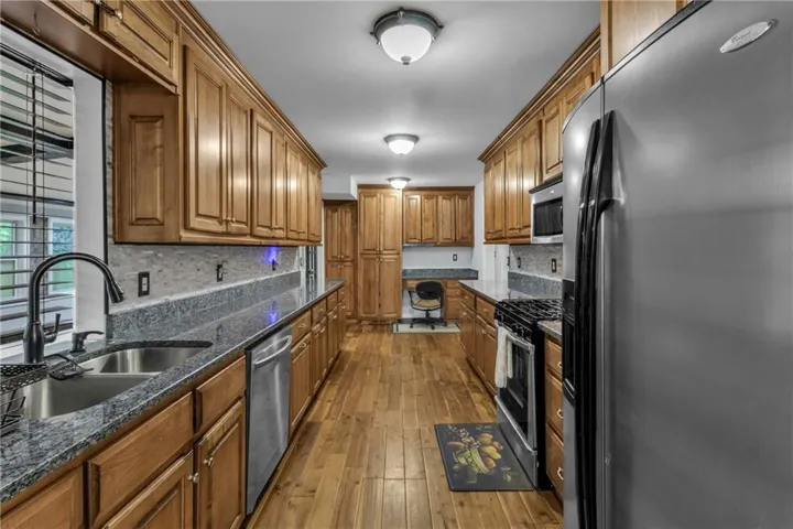 Galley kitchen featuring wood-finish flooring, wood cabinetry, granite countertops, and stainless steel appliances