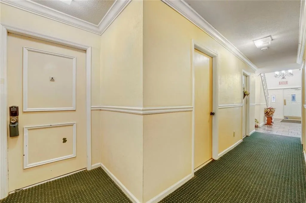 Hallway with a textured ceiling, crown molding, and dark colored carpet
