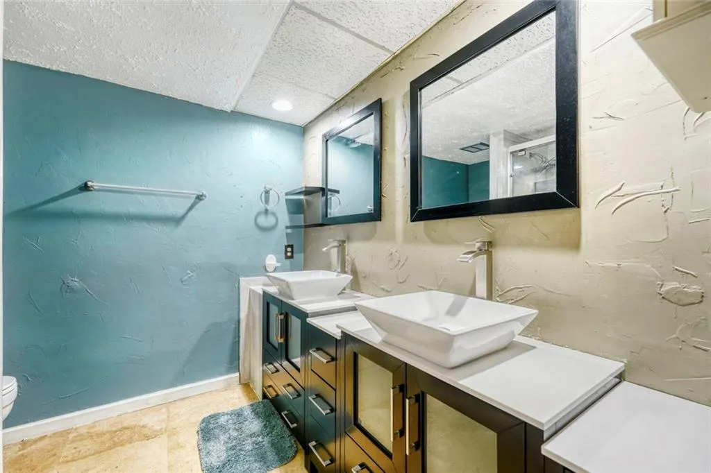 Full bath featuring a textured wall, double vanity, light tile patterned floors, a paneled ceiling, and a shower