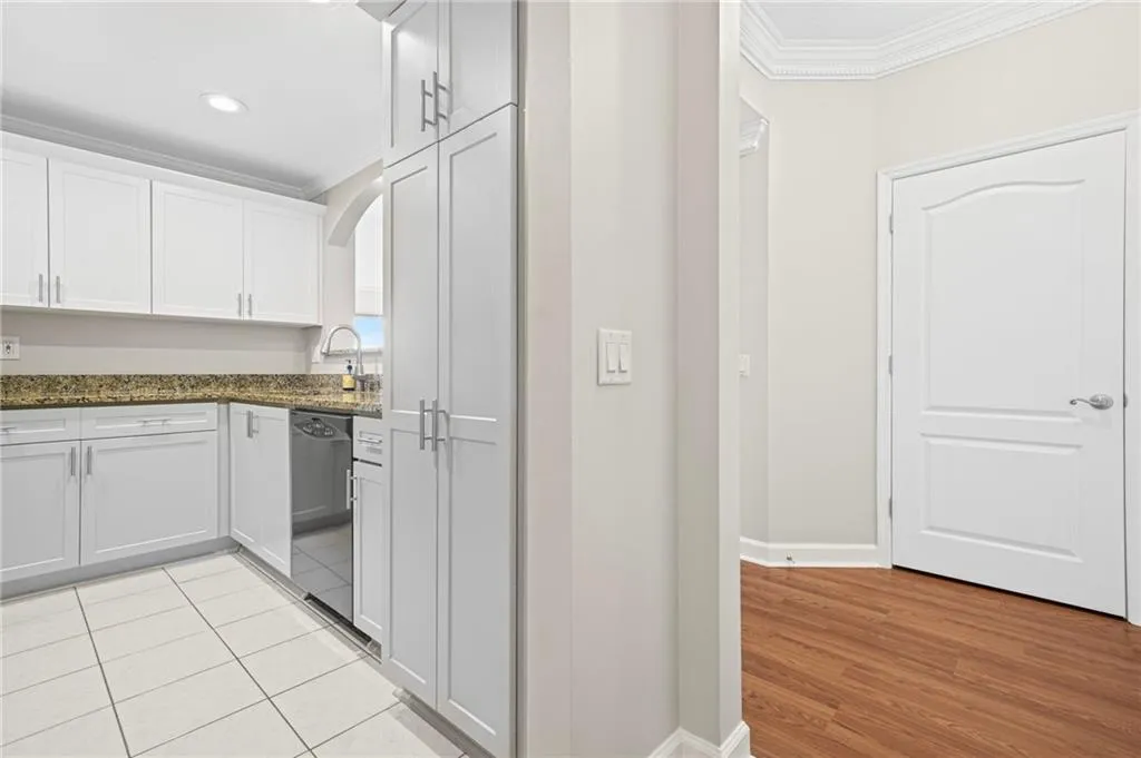 Kitchen featuring crown molding, dishwasher, white cabinetry, baseboards, and dark stone counters