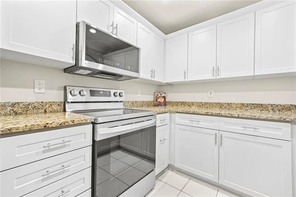 Kitchen featuring stainless steel appliances, light tile patterned floors, white cabinets, and light stone counters