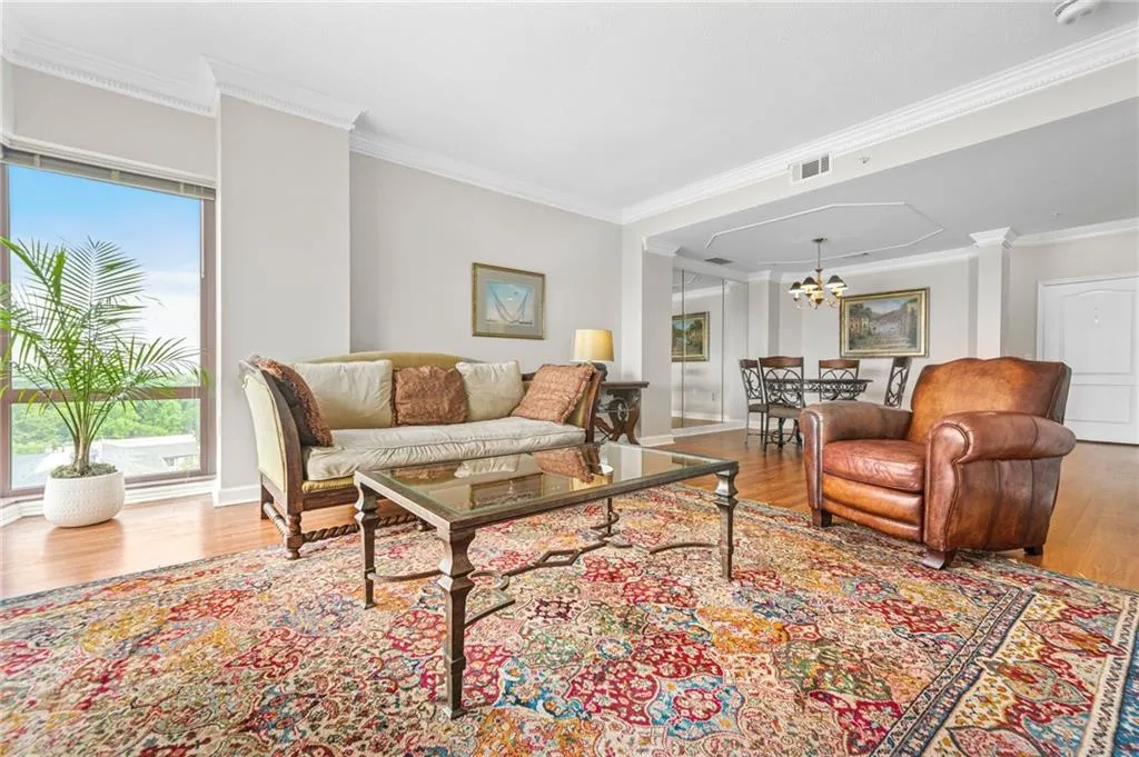 Living room featuring wood finished floors, a chandelier, ornamental molding, and baseboards